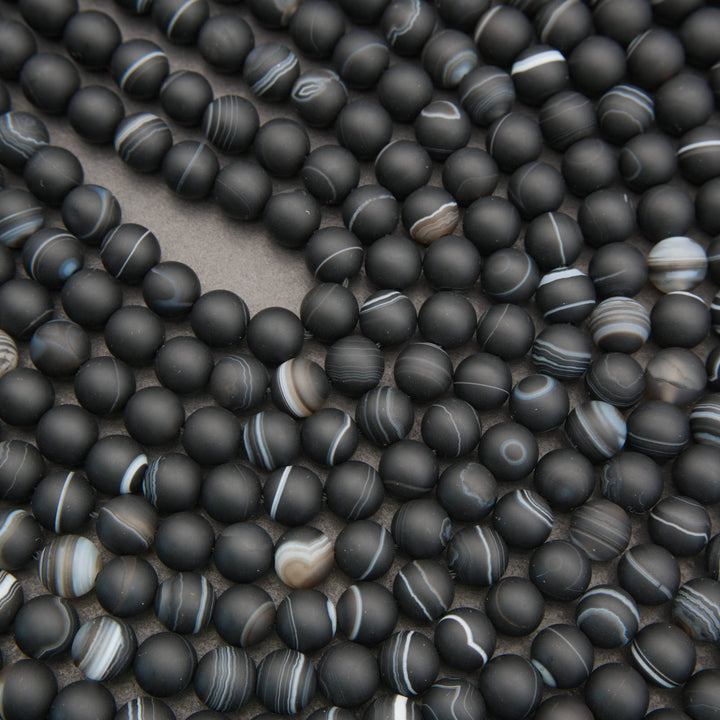 A close-up of many matte black round beads with some showing light gray and white banded striping, arranged on a neutral surface.