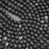 A close-up of many matte black round beads with some showing light gray and white banded striping, arranged on a neutral surface.