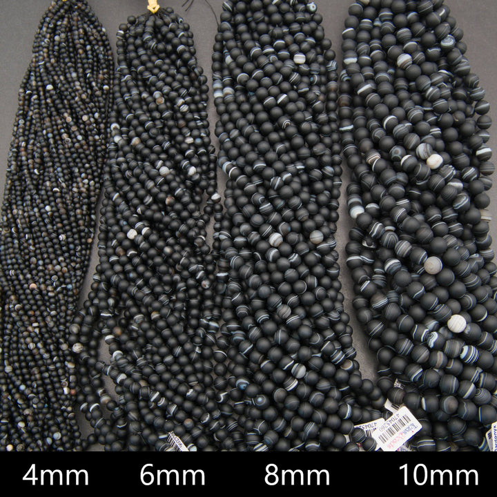 Four strands of black stone bead necklaces in 4mm, 6mm, 8mm, and 10mm sizes, laid out side-by-side on a dark background.