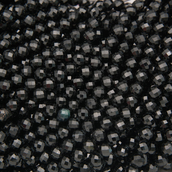 A close-up of many small faceted beads in a very dark charcoal/black color, with some reflective gray highlights and one slightly bluer bead near the lower center.