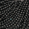 A close-up of many small faceted beads in a very dark charcoal/black color, with some reflective gray highlights and one slightly bluer bead near the lower center.