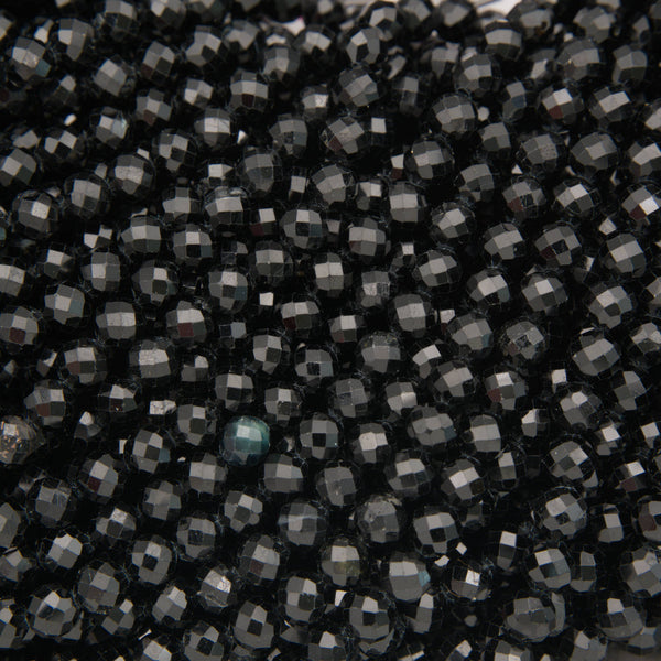 A close-up of many small faceted beads in a very dark charcoal/black color, with some reflective gray highlights and one slightly bluer bead near the lower center.