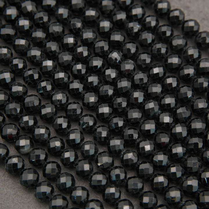 A close-up of many faceted round beads in a very dark charcoal/black color arranged in rows on a neutral gray surface.