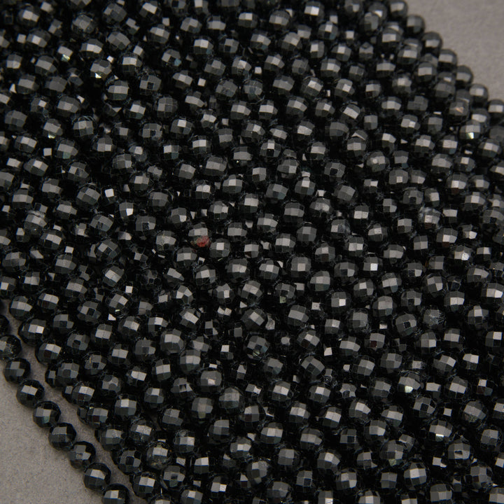Close-up of a pile of faceted black seed beads on a neutral gray background.