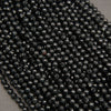 Close-up of a pile of faceted black seed beads on a neutral gray background.