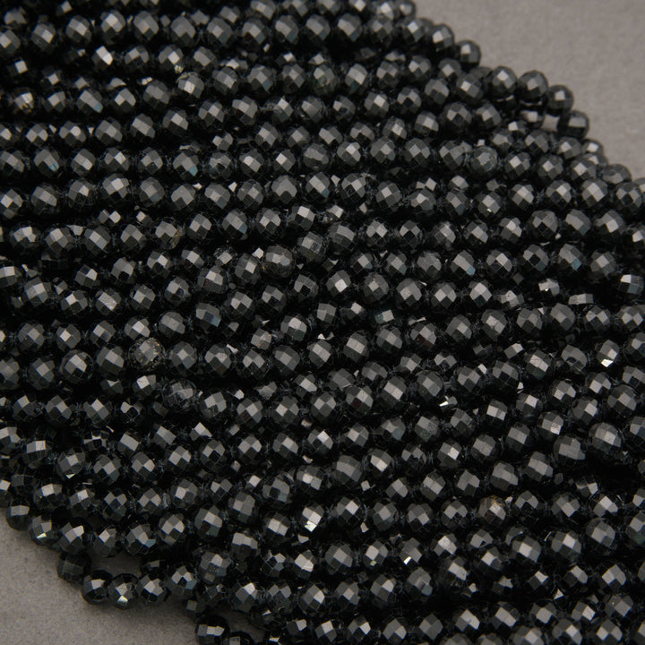 A close-up pile of small faceted black beads on a neutral gray background.