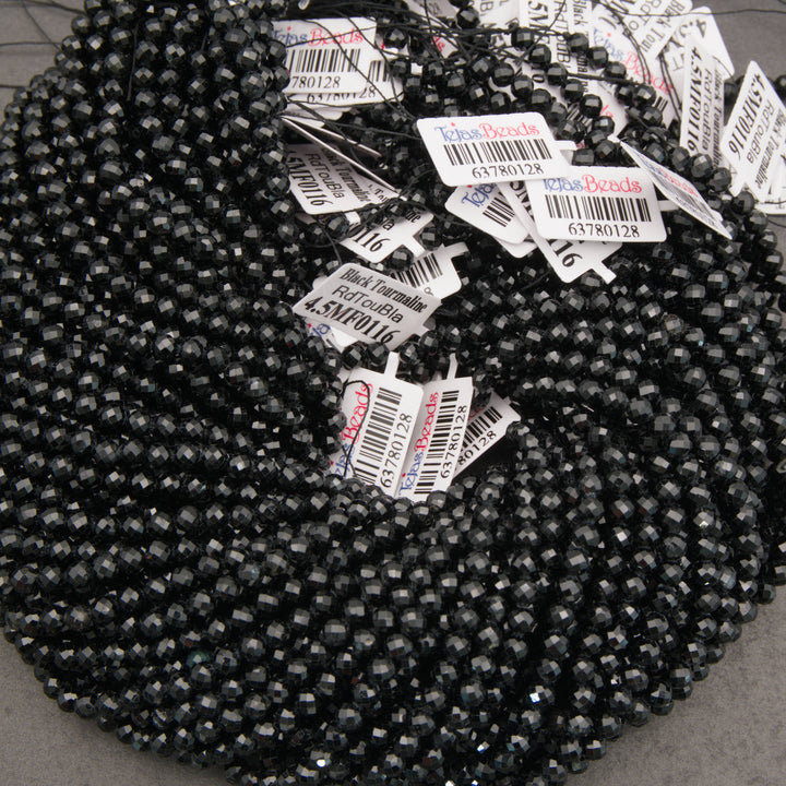 A large coil of faceted black seed beads with many white product tags attached, photographed on a neutral gray surface.