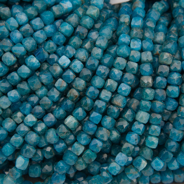 A close-up of strands of faceted turquoise-blue beads on a neutral gray background.