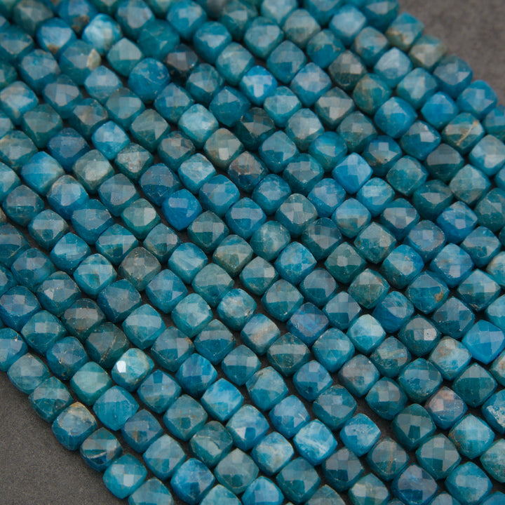 Close-up of multiple strands of faceted blue beads arranged diagonally on a dark gray surface.