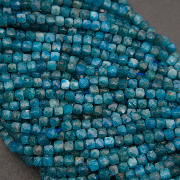 A close-up of strands of faceted turquoise-blue beads on a neutral gray background.