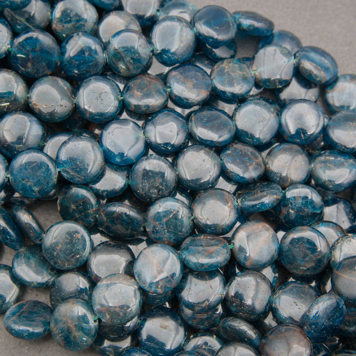 A close-up pile of round, polished blue glass beads with a glossy finish and natural mineral inclusions.