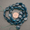 Blue polished stone beads with natural matrix inclusions, arranged in a circle around a US penny for scale on a neutral gray background.