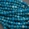 A close-up pile of round blue beads with natural marbled patterns in lighter turquoise and white.