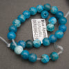 A strand of round blue apatite beads with natural marbling, shown coiled on a dark gray background with a white product tag in the center.