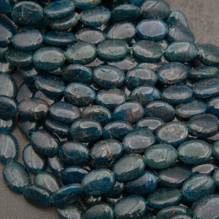 Strands of smooth oval blue apatite beads in dark teal with natural fracture lines
