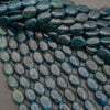 Smooth oval blue apatite bead strands laid diagonally, deep teal to dark ocean blue
