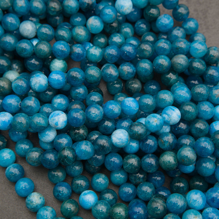 Close-up of a pile of smooth round blue apatite strands in deep teal and ocean blue, some beads with pale sky-blue marbling