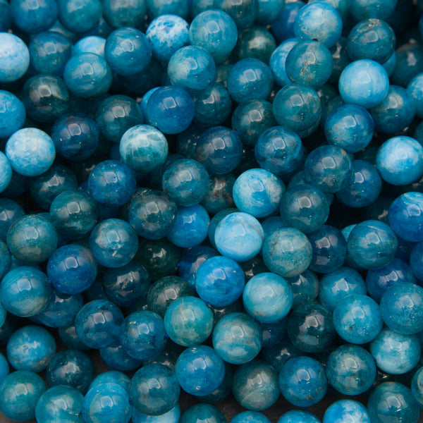 Close-up of a heap of smooth round blue apatite beads in deep teal and ocean blue with pale marbling