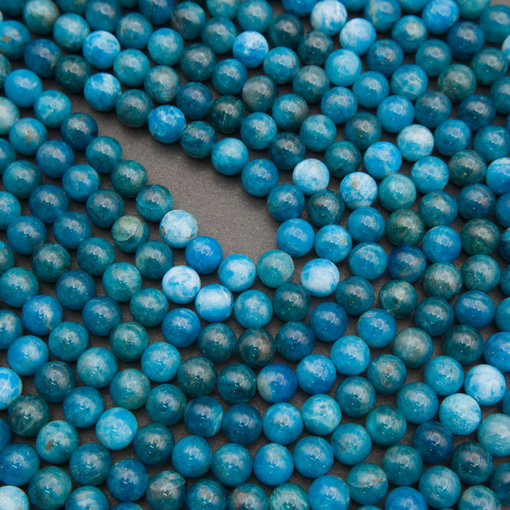 Strands of smooth round blue apatite beads laid in curving rows on a gray background, in teal, ocean blue and pale sky blue
