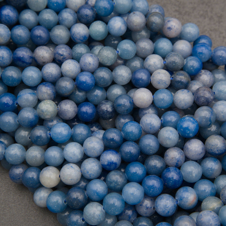 Strands of smooth round blue aventurine beads in rows on a gray background