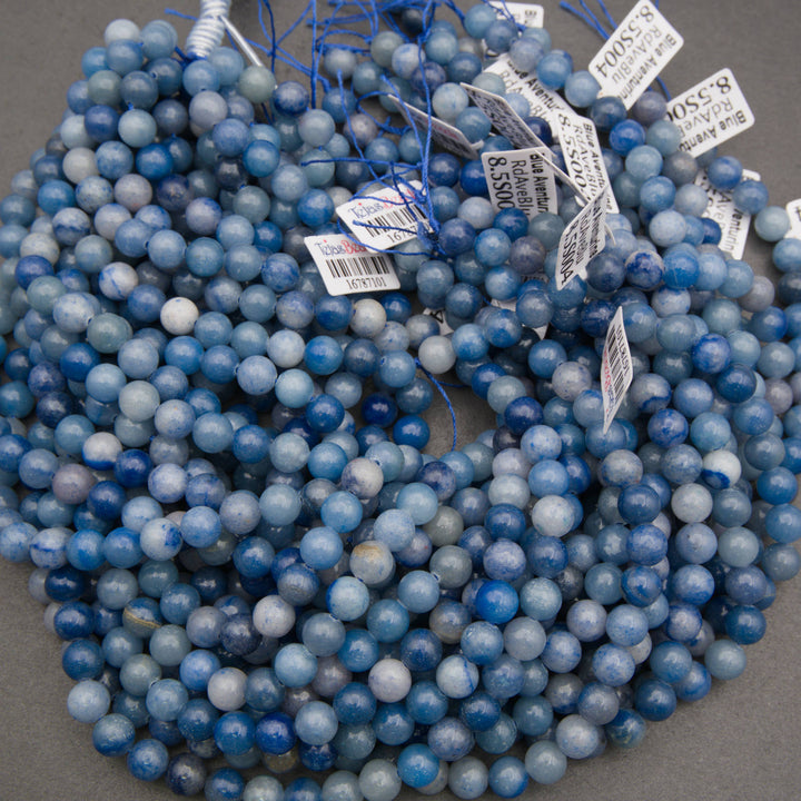 A bundle of smooth round blue aventurine bead strands with Tejas Beads tags