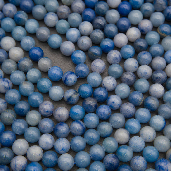 Rows of smooth round blue aventurine beads on a gray background in denim blue and pale blue