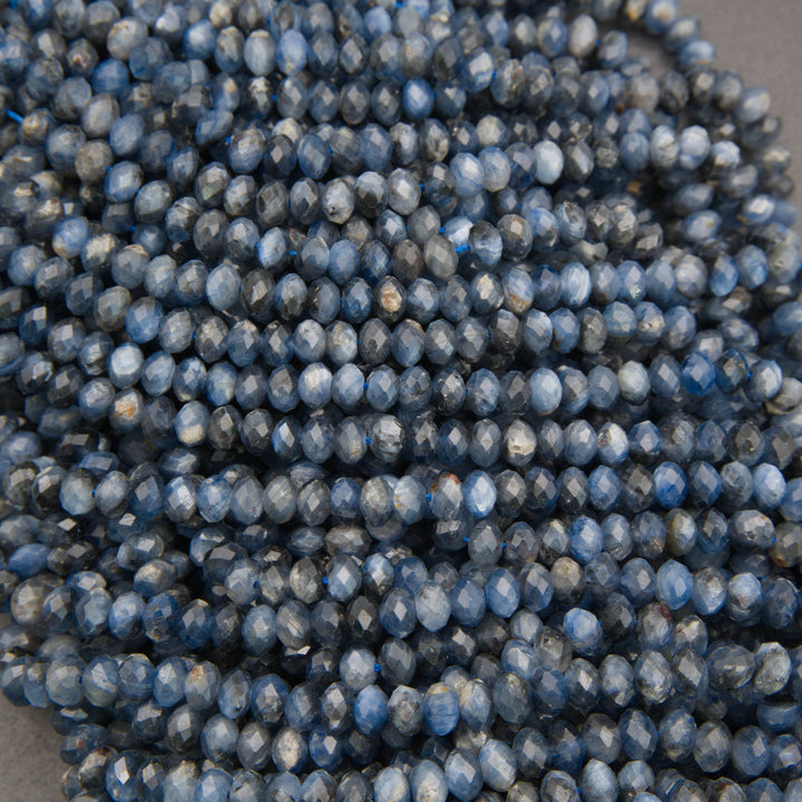 A close-up pile of faceted round beads in a blue-gray color with white marbling or cloudy inclusions, photographed against a dark neutral background.