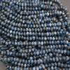 A close-up pile of faceted round beads in a blue-gray color with white marbling or cloudy inclusions, photographed against a dark neutral background.