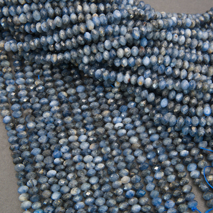 Close-up of multiple strands of faceted blue beads with natural marbling and white streaks, arranged on a neutral gray surface.