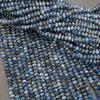 Close-up of multiple strands of faceted blue beads with natural marbling and white streaks, arranged on a neutral gray surface.