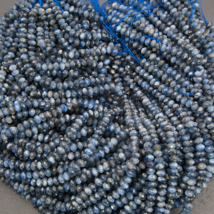 A pile of faceted round beads in a dusty slate blue color with white highlights, strung on thin blue cords.