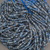 A pile of faceted round beads in a dusty slate blue color with white highlights, strung on thin blue cords.