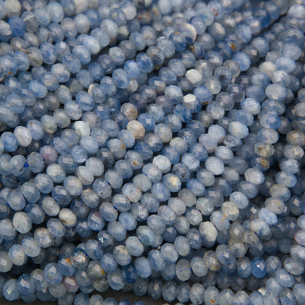 A close-up pile of faceted round gemstone beads in shades of light blue, medium blue, and white.