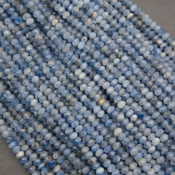 Close-up of multiple strands of faceted round beads in shades of light blue, medium blue, and white, arranged diagonally.