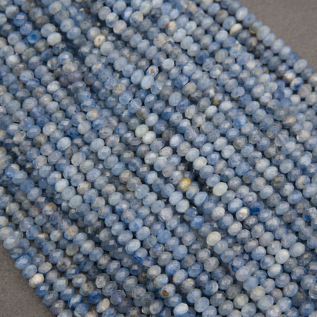 Close-up of multiple strands of faceted round beads in shades of light blue, medium blue, and white, arranged diagonally.