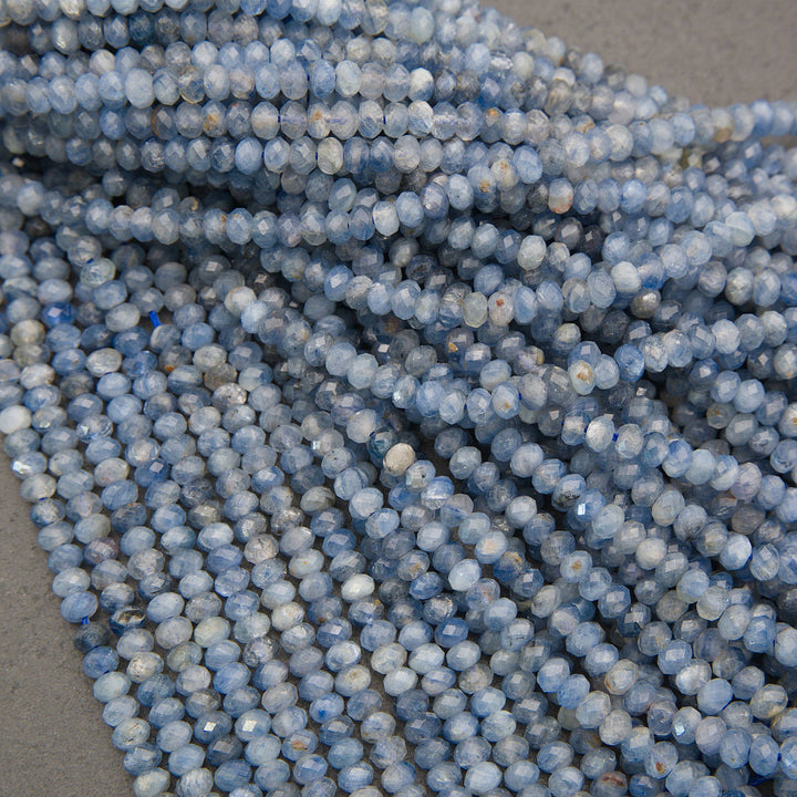 Close-up of multiple strands of faceted round beads in a light blue and white marbled pattern, arranged on a neutral gray surface.