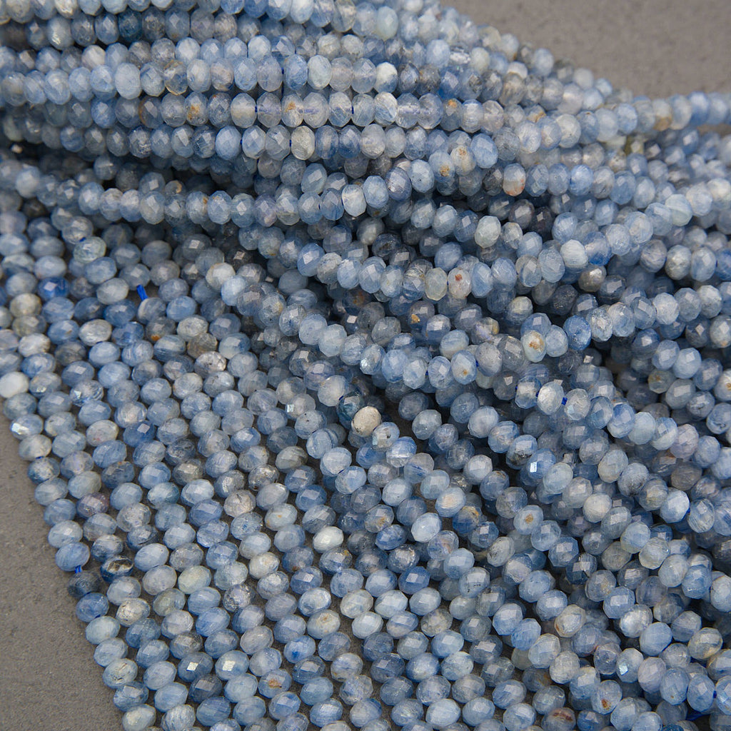 Close-up of multiple strands of faceted round beads in a light blue and white marbled pattern, arranged on a neutral gray surface.