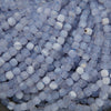 A close-up pile of faceted round beads in a pale icy blue and white marbled pattern.