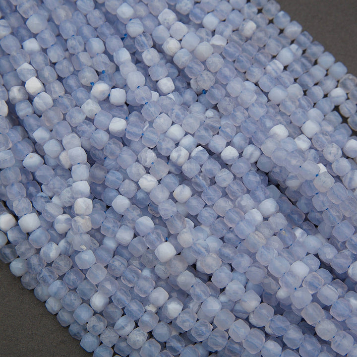 Close-up of strands of faceted pale blue beads with white cloudy highlights, arranged diagonally on a neutral gray surface.