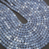 Coiled strands of faceted round beads in a pale icy blue and white marbled pattern, photographed close-up on a dark gray background.