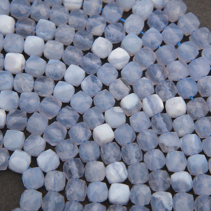 A close-up of faceted oval beads in a mix of pale blue, white, and light gray marbled tones, strung on thin blue cords.