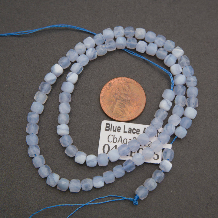 Blue lace agate beads on a dark gray background, shown with a copper penny for scale and a white label tag.