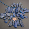 Blue sapphire teardrop beads strung on a blue cord, arranged in a circular pattern on a dark gray background with a penny for scale.