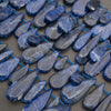 A close-up of polished blue teardrop-shaped gemstones strung along a bright blue cord, arranged in rows on a neutral surface.