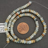 Necklace of multicolored beads with a penny for scale on a gray background