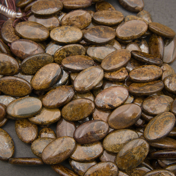 A heap of smooth oval bronzite bead strands with a bronze shimmer and patches of gray