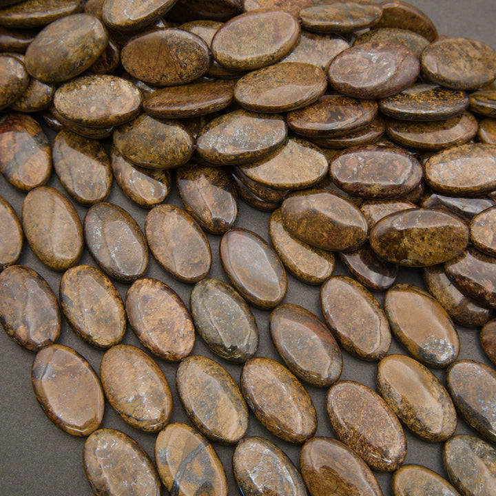 Rows of smooth oval bronzite beads on a gray background in warm bronze and golden brown