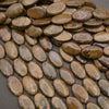 Rows of smooth oval bronzite beads on a gray background in warm bronze and golden brown