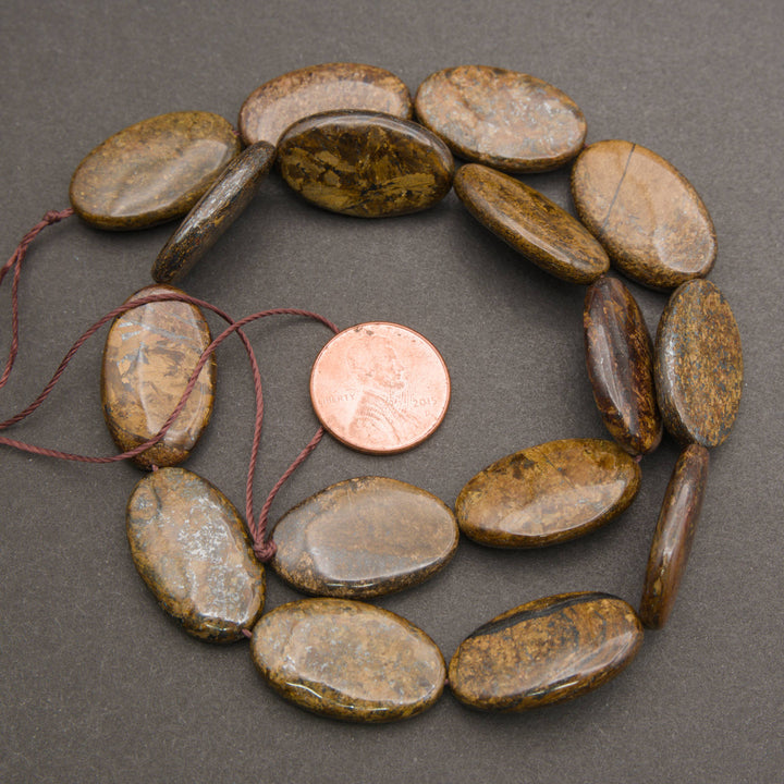 A strand of smooth oval bronzite beads coiled around a penny for scale