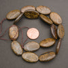 A strand of smooth oval bronzite beads coiled around a penny for scale